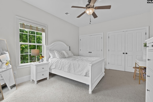 bedroom with multiple closets, light carpet, ceiling fan, and baseboards