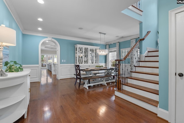 dining room with arched walkways, wainscoting, stairs, dark wood-style floors, and crown molding
