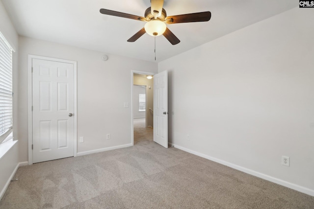 unfurnished bedroom featuring light carpet, multiple windows, baseboards, and ceiling fan