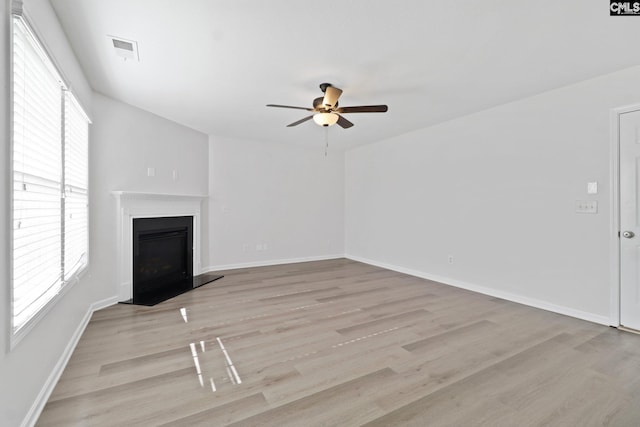 unfurnished living room with a ceiling fan, light wood-type flooring, healthy amount of natural light, and a fireplace with raised hearth