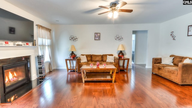 living room with a ceiling fan, a glass covered fireplace, wood finished floors, and baseboards
