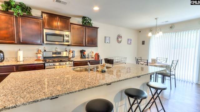 kitchen featuring appliances with stainless steel finishes, a sink, a breakfast bar area, light wood-style flooring, and light stone counters