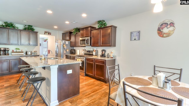 kitchen with stainless steel appliances, a sink, a breakfast bar area, light wood finished floors, and recessed lighting