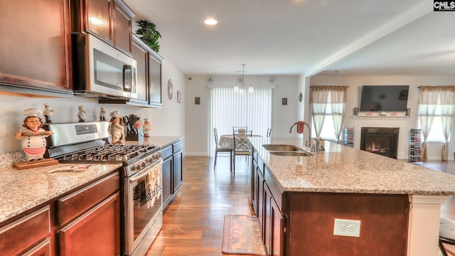 kitchen featuring appliances with stainless steel finishes, a sink, open floor plan, a chandelier, and wood finished floors