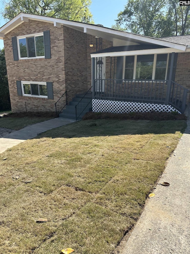 view of front facade with brick siding, a front yard, and a sunroom