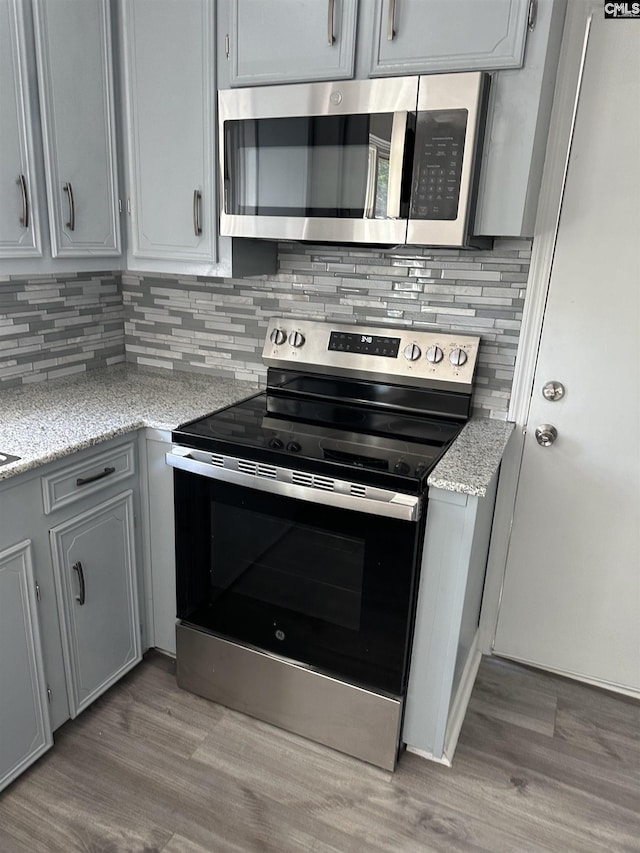kitchen featuring appliances with stainless steel finishes, light wood finished floors, backsplash, and light stone countertops