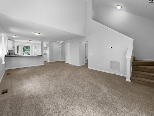 unfurnished living room with carpet flooring, stairway, baseboards, and a high ceiling