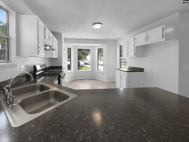 kitchen with a sink, stainless steel gas range, under cabinet range hood, plenty of natural light, and a textured ceiling