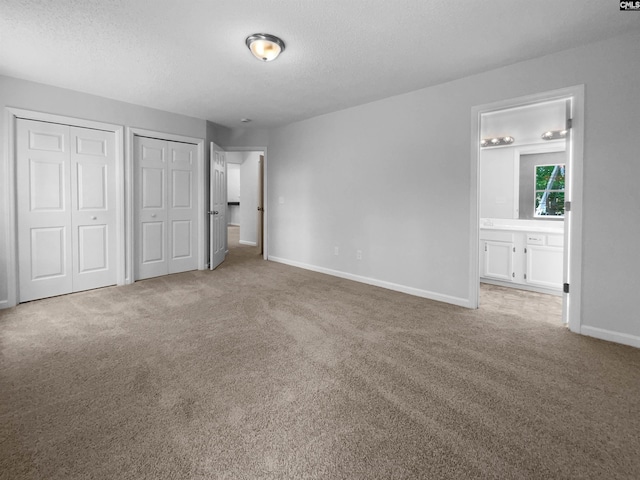 unfurnished bedroom with two closets, carpet flooring, baseboards, a textured ceiling, and connected bathroom