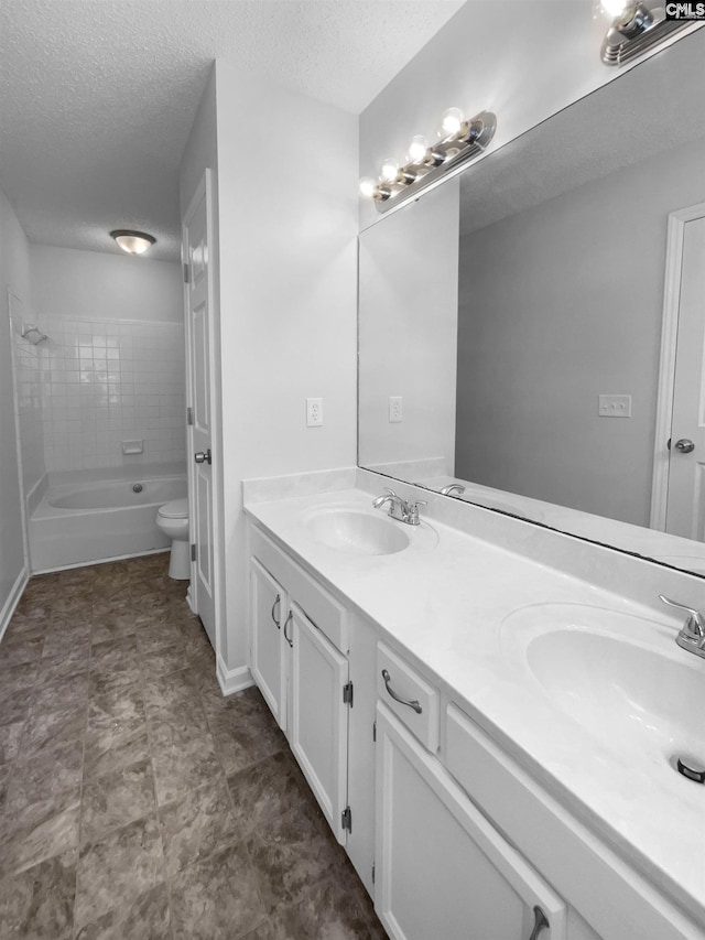 full bath with toilet, a textured ceiling, double vanity, bathing tub / shower combination, and baseboards