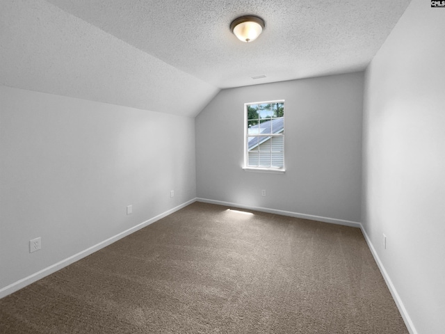 additional living space featuring a textured ceiling, carpet flooring, baseboards, and vaulted ceiling