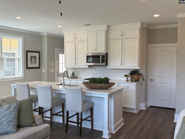 kitchen featuring stainless steel microwave, crown molding, backsplash, dark wood-style flooring, and white cabinetry
