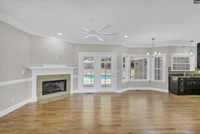 unfurnished living room with light wood-type flooring, crown molding, a premium fireplace, a chandelier, and a ceiling fan