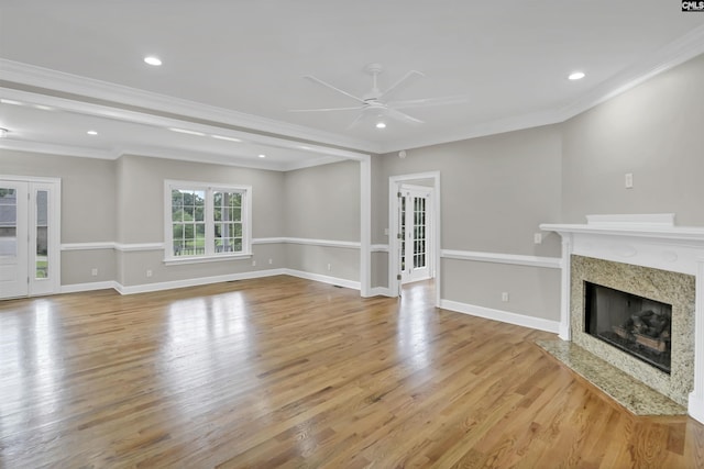 unfurnished living room with a ceiling fan, a fireplace, crown molding, light wood-style floors, and french doors