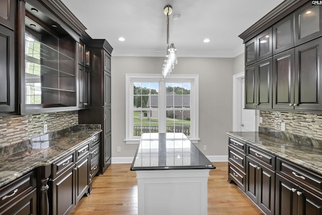 kitchen with decorative backsplash, dark stone countertops, hanging light fixtures, crown molding, and glass insert cabinets