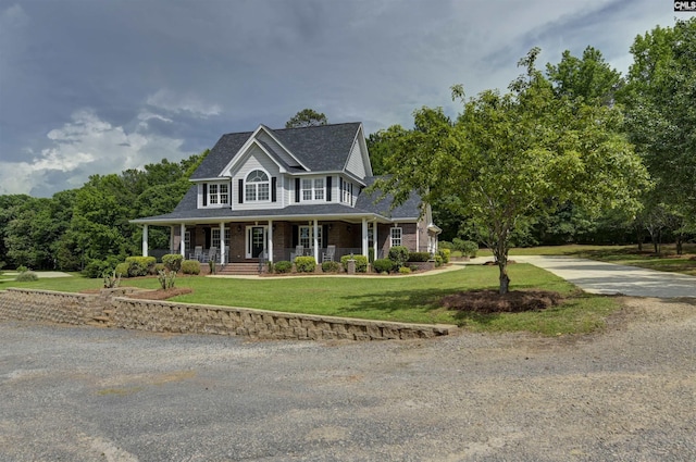 colonial house with a porch, driveway, a front lawn, a shingled roof, and brick siding