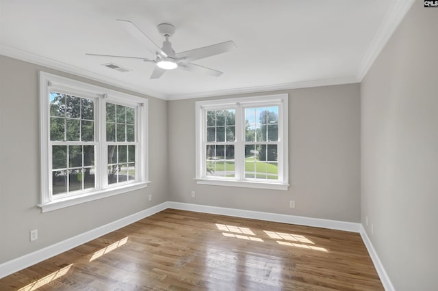 empty room with crown molding, healthy amount of natural light, baseboards, ceiling fan, and wood finished floors
