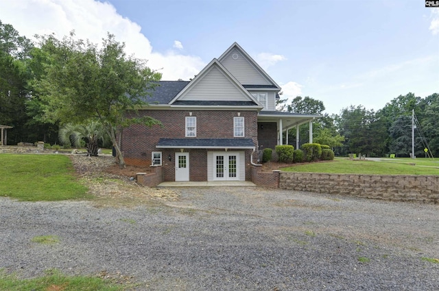 view of front of home featuring french doors, brick siding, a front lawn, and gravel driveway