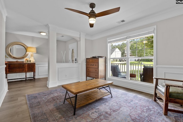 living room with a decorative wall, a ceiling fan, wood finished floors, a wainscoted wall, and crown molding
