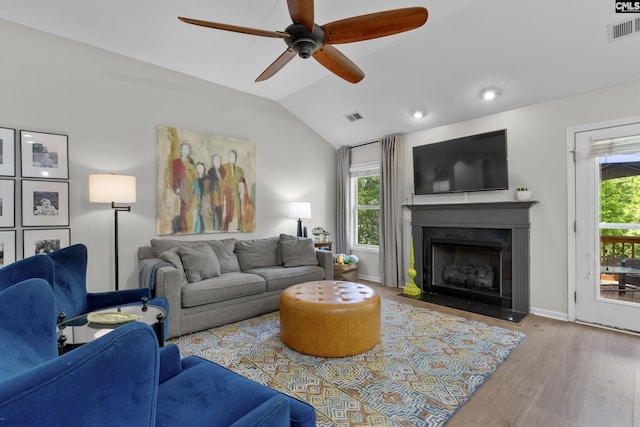 living area with a ceiling fan, wood finished floors, lofted ceiling, healthy amount of natural light, and a fireplace with flush hearth