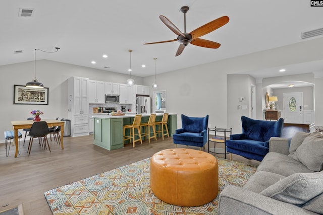 living area featuring a ceiling fan, arched walkways, light wood finished floors, recessed lighting, and lofted ceiling