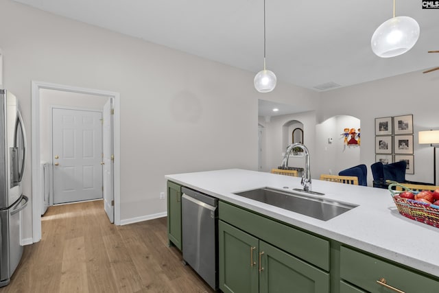 kitchen with green cabinets, stainless steel appliances, a sink, light wood-style flooring, and pendant lighting