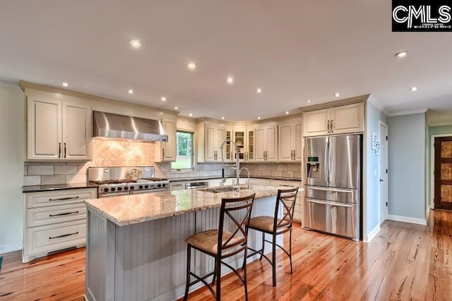 kitchen featuring stainless steel fridge, range, wall chimney exhaust hood, a sink, and crown molding