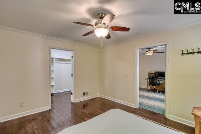 bedroom with an office area, wood finished floors, crown molding, a spacious closet, and baseboards
