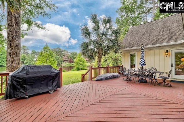 wooden terrace with outdoor dining area, a grill, a water view, and a lawn
