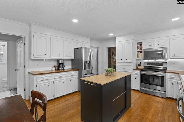 kitchen with appliances with stainless steel finishes, wood counters, ornamental molding, white cabinetry, and backsplash