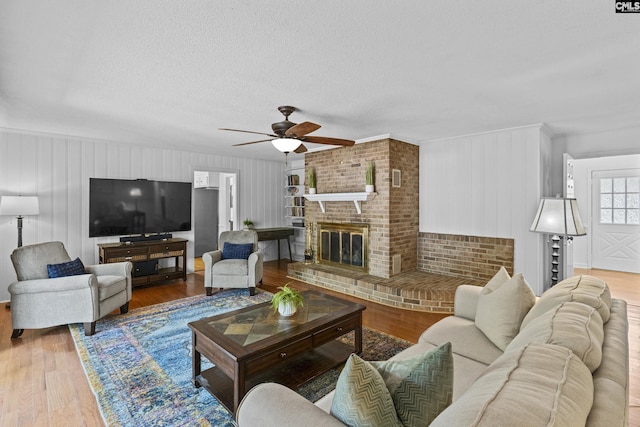 living area with ceiling fan, wood finished floors, a brick fireplace, ornamental molding, and a textured ceiling