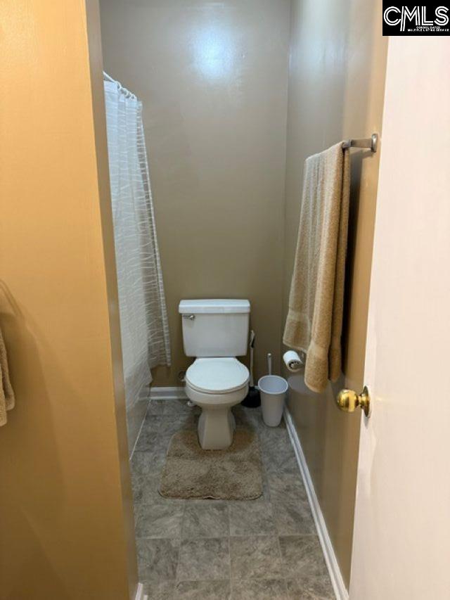 bathroom with toilet, a shower with shower curtain, and baseboards
