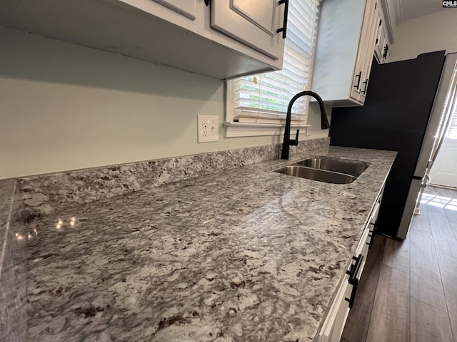 kitchen featuring a sink, dark wood-style flooring, light stone counters, white cabinetry, and freestanding refrigerator
