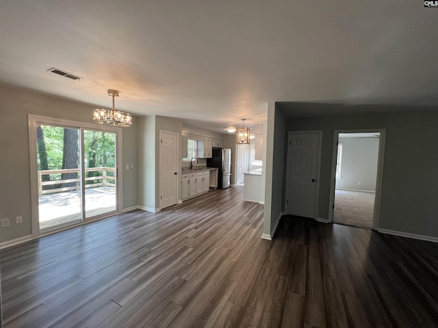 unfurnished living room with a chandelier, baseboards, and dark wood finished floors