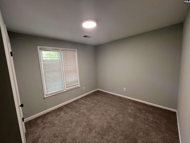 empty room featuring dark colored carpet and baseboards