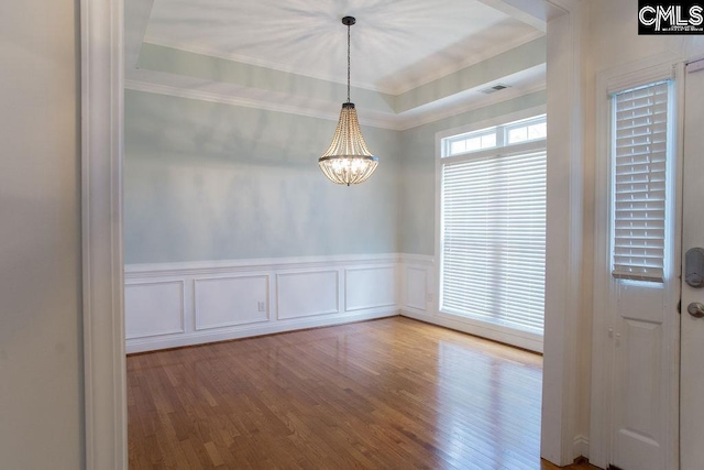 unfurnished dining area with ornamental molding, a chandelier, wood finished floors, wainscoting, and a decorative wall