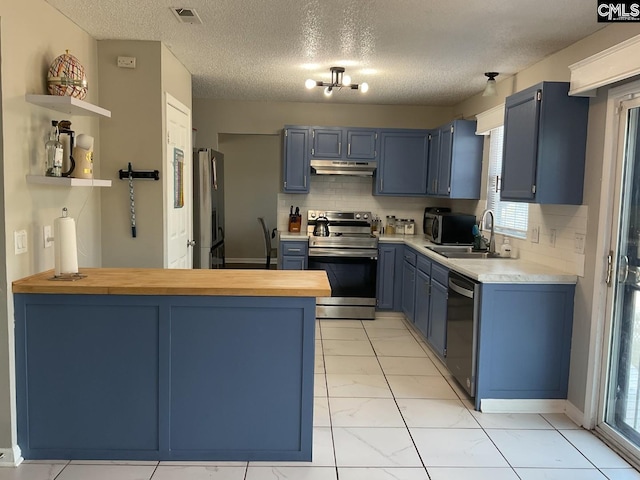 kitchen featuring stainless steel range with electric cooktop, blue cabinets, under cabinet range hood, dishwashing machine, and freestanding refrigerator