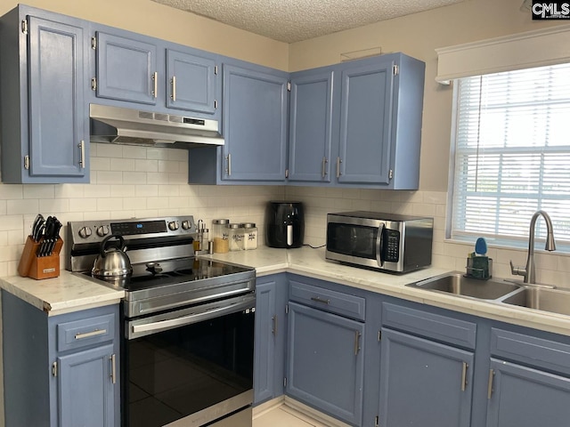 kitchen featuring stainless steel appliances, under cabinet range hood, blue cabinets, and a textured ceiling