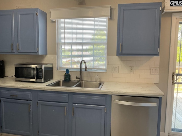 kitchen featuring stainless steel appliances, a sink, tasteful backsplash, light countertops, and blue cabinetry