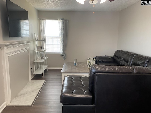 living room featuring a textured ceiling, a ceiling fan, dark wood-type flooring, and baseboards