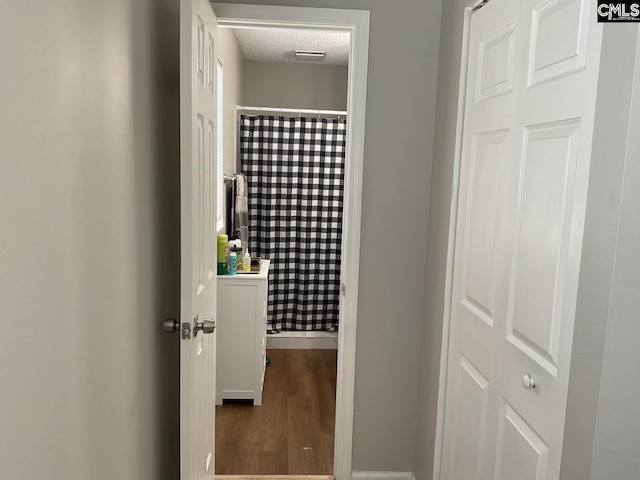hallway with baseboards, wood finished floors, and a textured ceiling
