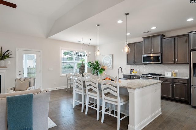 kitchen with appliances with stainless steel finishes, dark brown cabinetry, dark wood-style floors, backsplash, and a kitchen bar