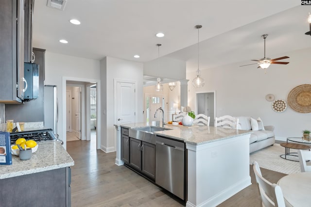 kitchen featuring stainless steel dishwasher, a sink, baseboards, open floor plan, and light wood-style floors