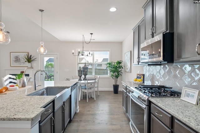 kitchen with stainless steel appliances, a sink, wood finished floors, baseboards, and backsplash
