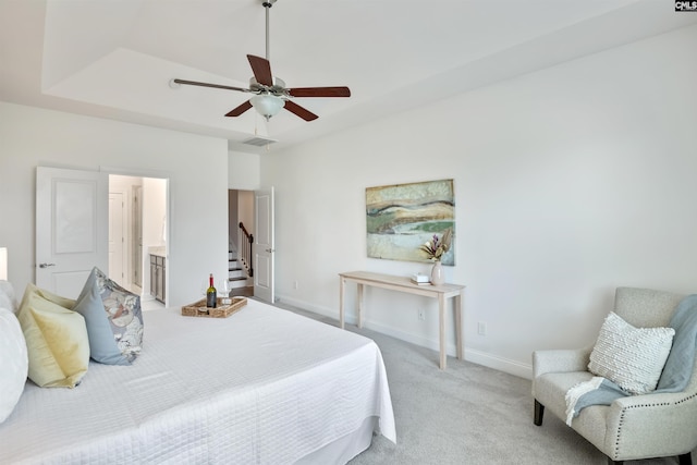 bedroom with light colored carpet, baseboards, a tray ceiling, a ceiling fan, and connected bathroom
