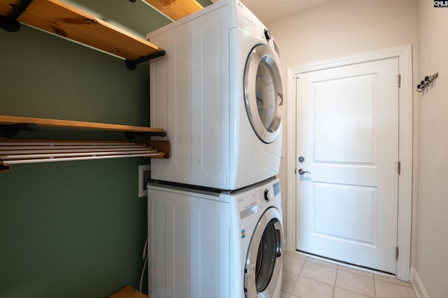 laundry room with stacked washer / drying machine, light tile patterned flooring, and baseboards