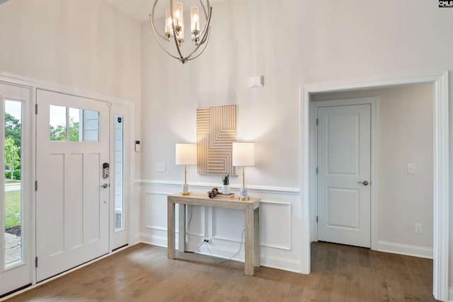 entryway featuring wood finished floors, a chandelier, a wainscoted wall, and a towering ceiling
