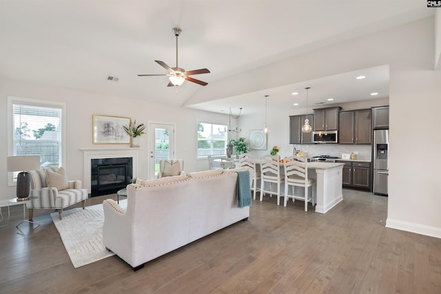 living area featuring wood finished floors, a glass covered fireplace, ceiling fan, recessed lighting, and vaulted ceiling