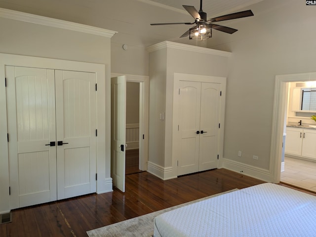 unfurnished bedroom with wood finished floors, baseboards, two closets, crown molding, and ensuite bath