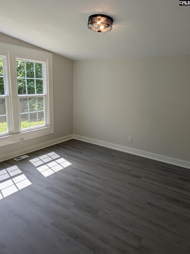 empty room with dark wood-style flooring, baseboards, and vaulted ceiling